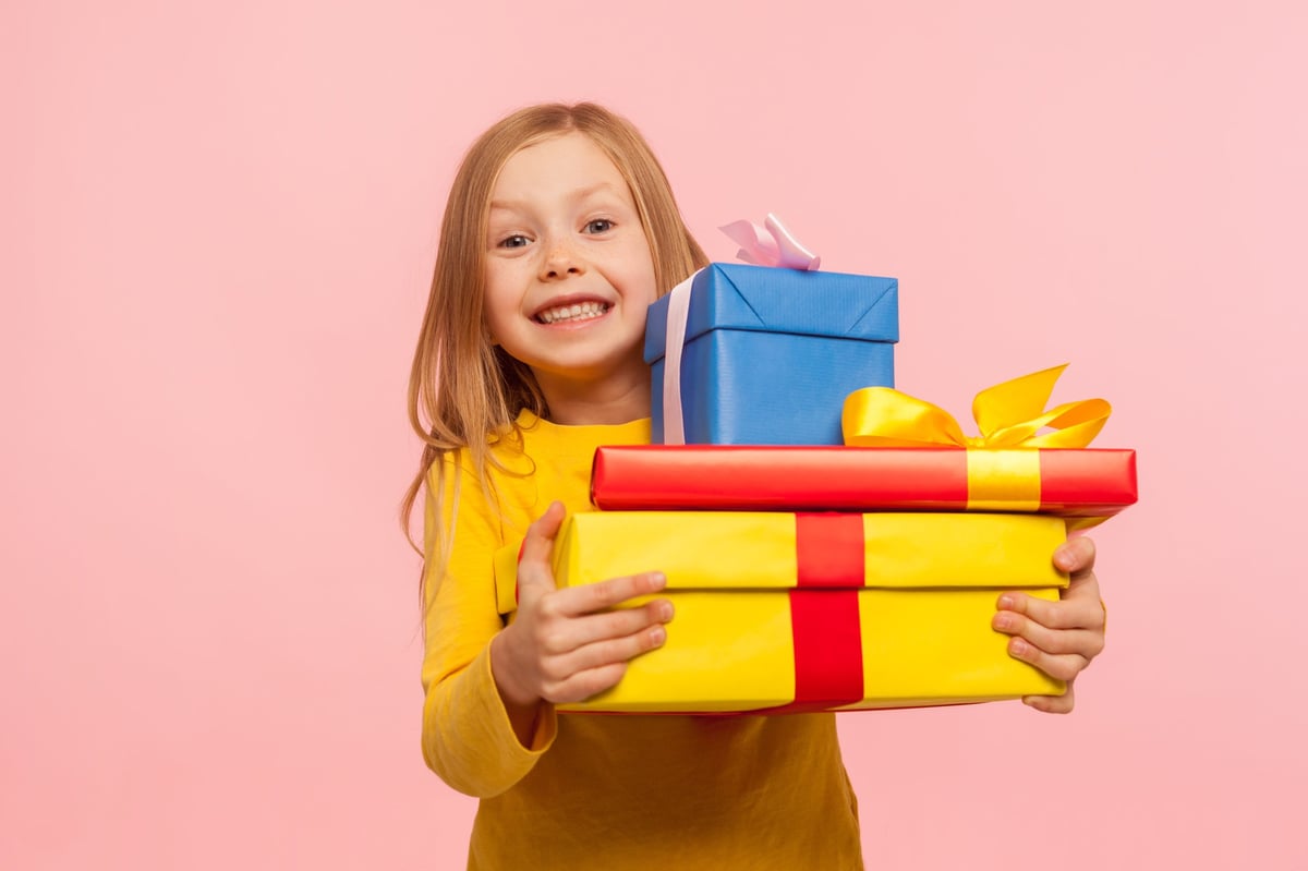 A delighted little girl hugging a stack of gift boxes and smiling