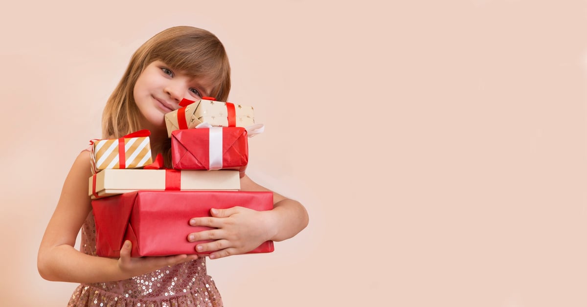 A little girl in a beautiful dress holding a stack of brightly coloured gift boxes