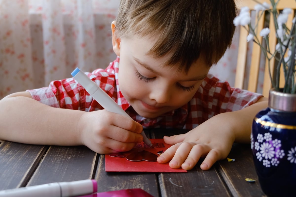 A little boy making a handmade card, concentrating on his artwork